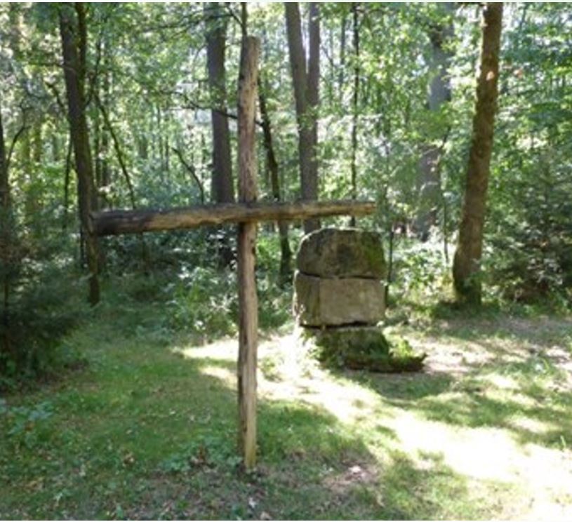 Foto, aufgenommen im Wald, mit einem Kreuz aus Baumstämmen und einem Altar aus Steinen
