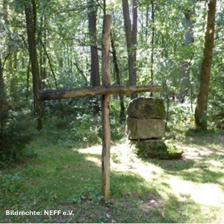Foto, aufgenommen im Wald, mit einem Kreuz aus Baumstämmen und einem Altar aus Steinen
